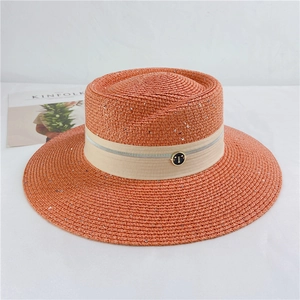 Detailed macro of orange straw sun hat featuring sparkling sequins and a metallic 'T' buckle