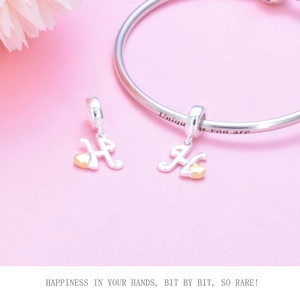 Macro detail of S925 silver letter H charm with gold heart on snake chain bracelet