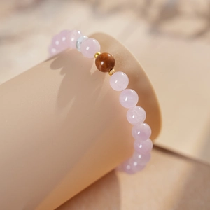 Close-up of pink beaded bracelet with brown accent bead on a soft cream display stand