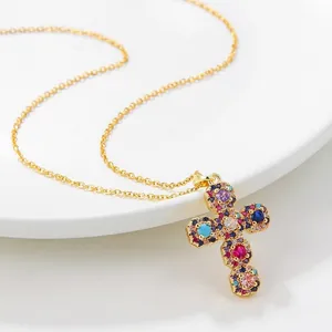 Élégant collier croix en titane doré avec zircons colorés sur une assiette en porcelaine