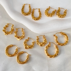 Detail view of various twisted gold hoop earrings on a white satin fabric background