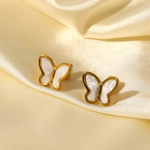 Dettaglio macro degli orecchini a farfalla dorati 18K con conchiglia bianca su seta champagne
