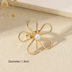 Detailed view of a gold flower ring with a white pearl center on a neutral textured surface