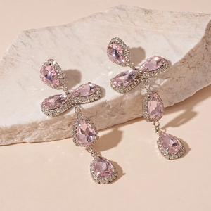 Detailed view of pink teardrop rhinestones on long silver tassel earrings over white stone