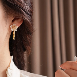 Detail of model wearing gold shell flower earrings with zircon key pendant