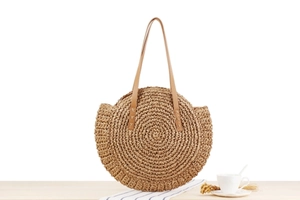 Detail of round paper rope woven bag with brown leather straps on a wooden table
