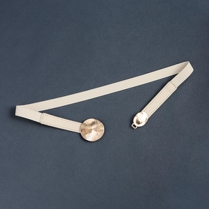 Detail of light beige elastic belt featuring a textured gold circular metal buckle