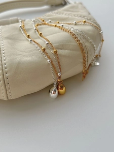 Close-up of minimalist gold and silver teardrop pendant necklaces on a beige leather bag