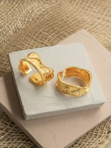 Detail of two golden irregular textured rings showing lava style ripple on stone stand