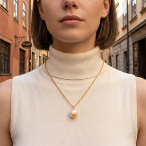 Close-up of elegant 18K gold pearl pendant necklace on a model with vintage street background
