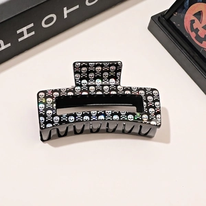 Detail of a black square hair claw clip featuring a holographic skull and crossbones print
