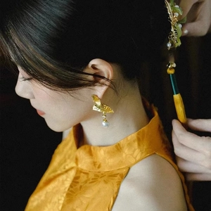 Boucles d'oreilles éventail dorées avec perles de style chinois portées par un mannequin