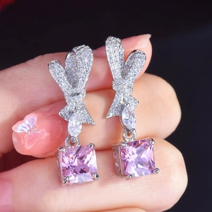 Pink radiant cut diamond drop earrings with silver bow design held by hand
