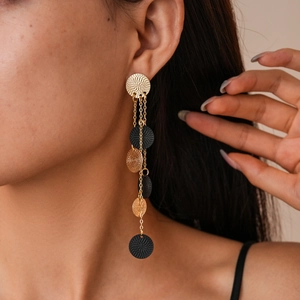 Detail view of long tassel drop earrings with textured gold and black circular charms