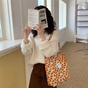 Close-up of floral corduroy tote bag with orange flowers held by a model in a cozy setting