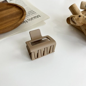 Detailed macro view of a matte light brown hair claw clip on a minimalist wooden background
