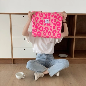 Pink leopard print canvas tote bag with a white woven label held by a model on wood floor