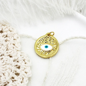 Macro view of gold evil eye charm with blue enamel on white feather background