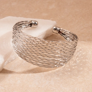 Detail of silver wavy multilayer open bangle cuff on a white natural stone prop