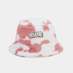 Détail d'un bob en fausse fourrure rose à motif vache avec écusson brodé CUTE arc-en-ciel