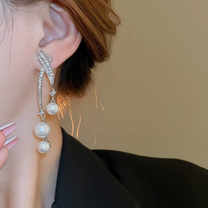 Détail de boucles d'oreilles pendantes argentées avec diamants et trois perles sur mannequin