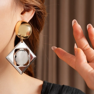 Macro view of gold and silver contrast geometric earrings worn on a model ear