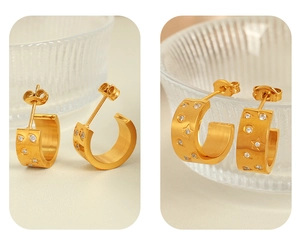 Macro detail of gold C-shaped hoop earrings with embedded star and round zircon stones