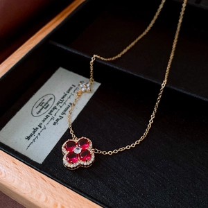 Macro shot of gold necklace featuring red zircon four-leaf clover pendant on black box