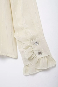 Close-up of ruffled cuffs with silver buttons and metallic stripes on a beige blouse