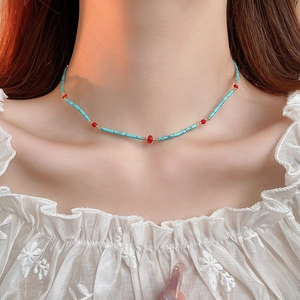Detail of bohemian turquoise beaded necklace with red accents on model collarbone