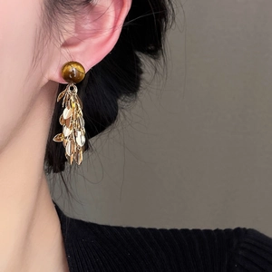 Detail of tiger eye stone earrings with golden leaf tassels on a female model