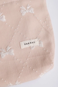 Dettaglio del beauty case rosa con fiocco in rilievo, motivo a pois e logo H&R BAG