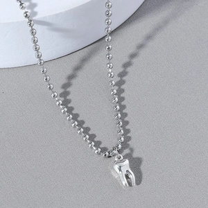 Silver bead chain necklace with 3D tooth pendant displayed on a textured grey surface