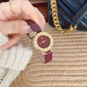 Close-up of a women's watch with burgundy leather strap and golden case held in hand