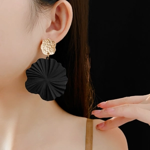 Close-up of model wearing gold pleated metal and black irregular wavy earrings