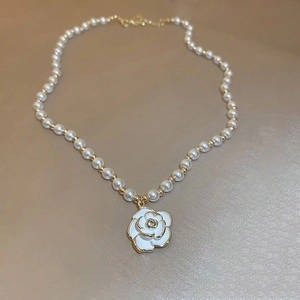 Detailed close-up of pearl necklace featuring a white enamel camellia flower pendant