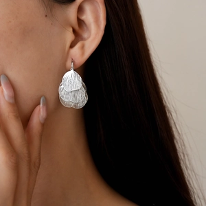 Close-up of silver hollow heart-shaped petal earrings with multi-layered metal texture