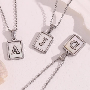 Macro shot of silver letter pendants A, J, D with white shell inlay on wet background