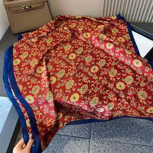 Detailed flat lay of red peony print silk scarf with golden floral patterns and blue hem