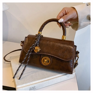 Detail of vintage dark brown faux leather handbag with gold buckle and bell pendant