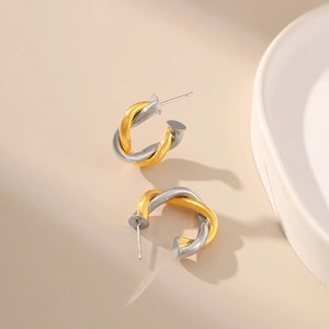 Detail of two-tone twisted knot earrings in gold and silver finish on warm beige background