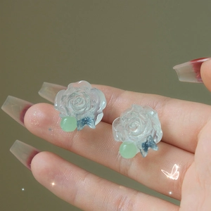 Macro shot of resin flower and butterfly stud earrings held on a finger