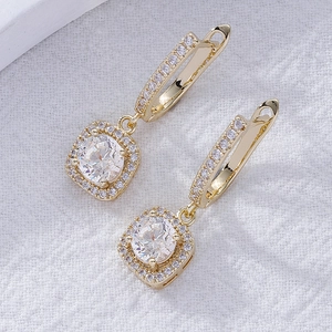 Gold halo drop earrings with round center stone and lever-back hooks on white fabric