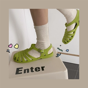 Close-up of green Roman woven jelly sandals with metal buckle and white socks