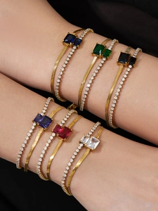 Detail of double-layered gold bracelets with rectangular colored crystals on black backdrop