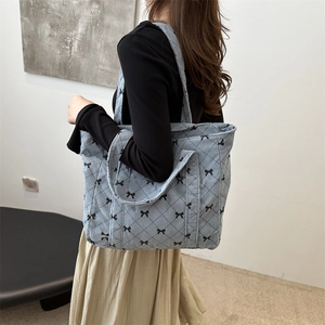 Blue corduroy tote bag with black bow patterns and diamond quilting on a female model