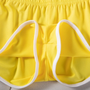 Detail der gelben Sportshorts mit atmungsaktivem Mesh-Gewebe und weißer Saumnaht