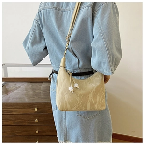 Détail du sac hobo plissé beige avec pendentif perle porté par un mannequin