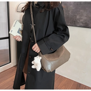 Deep khaki PU leather hobo bag with a plush bear charm worn by a model in black coat