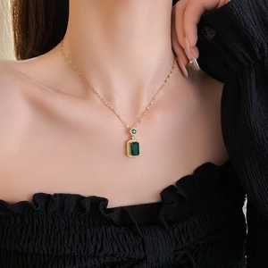 Close-up of a vintage gold chain necklace with a square emerald pendant on a model